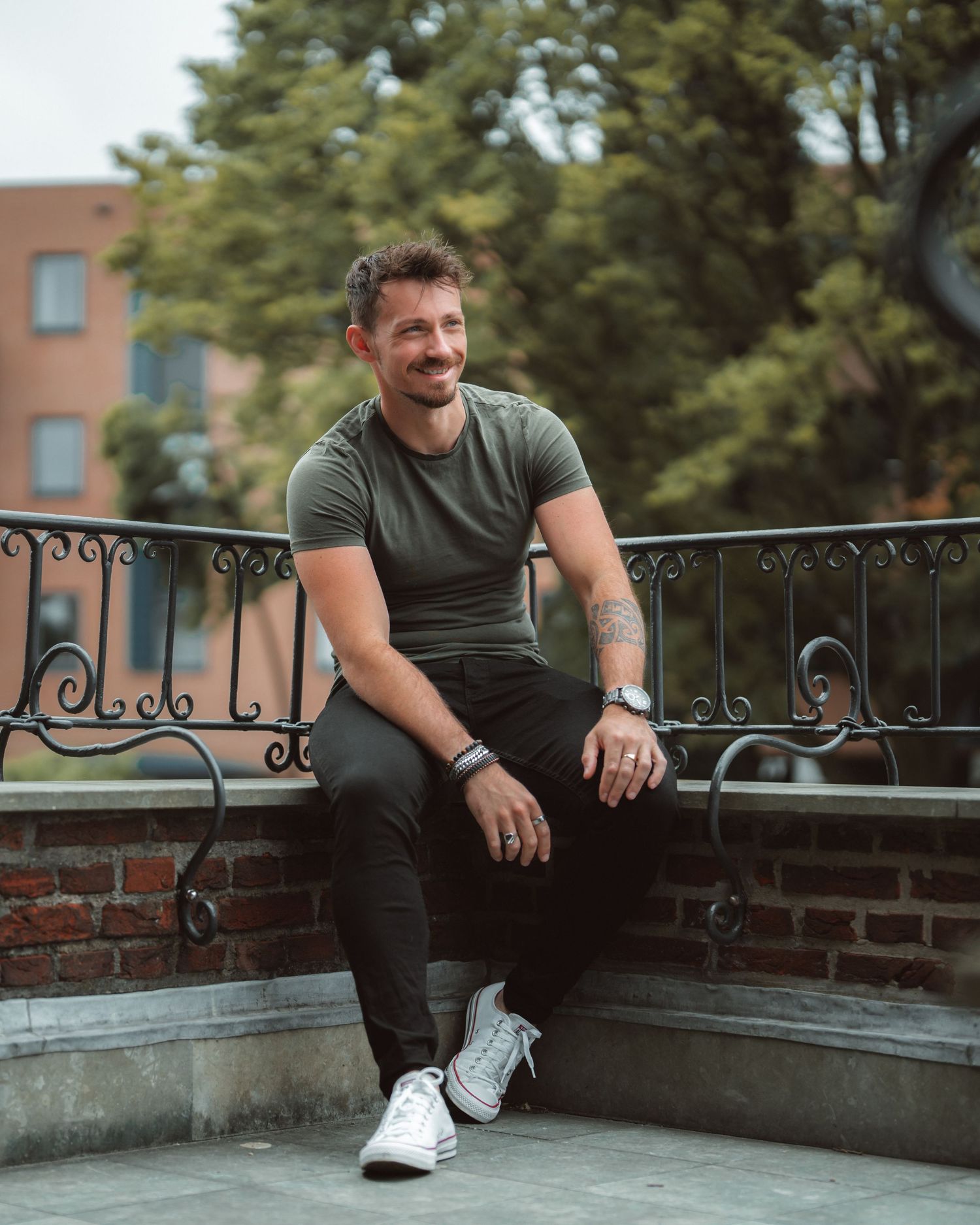 Person in casual attire sitting on brick wall with decorative railing outdoors.