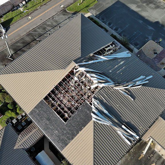 Aerial view of severe roof damage showing collapsed sections and exposed structure.