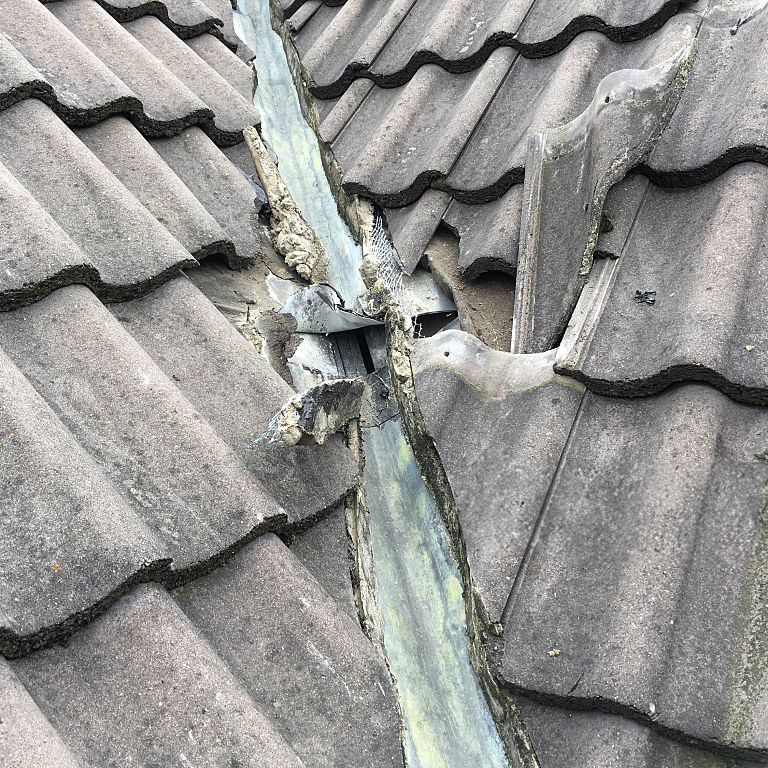 Close-up of damaged roof valley showing deteriorated metal flashing and tiles.