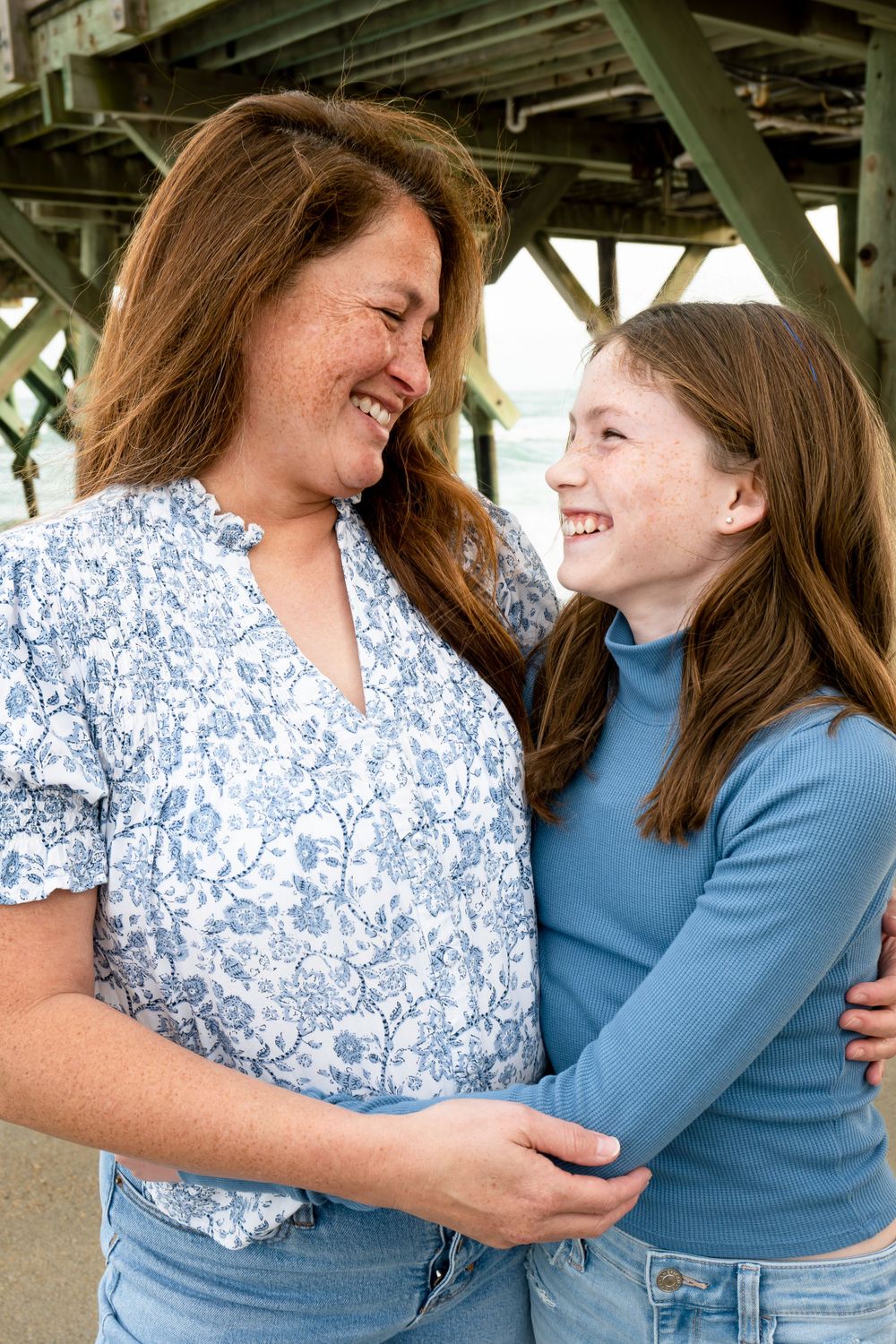 Two people sharing a joyful moment together under a pier at the beach.