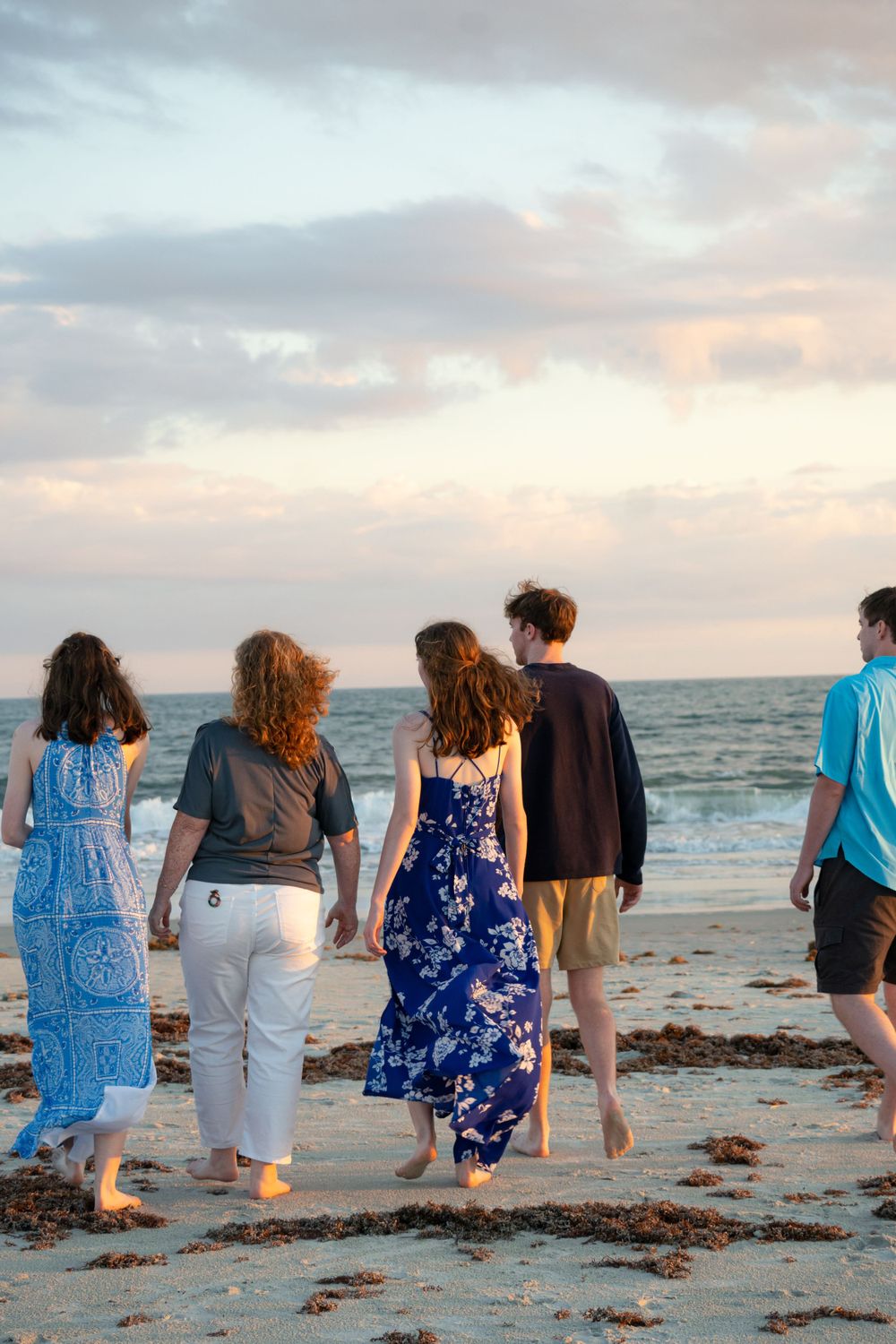 Beachgoers walking along shoreline at sunset with ocean waves.
