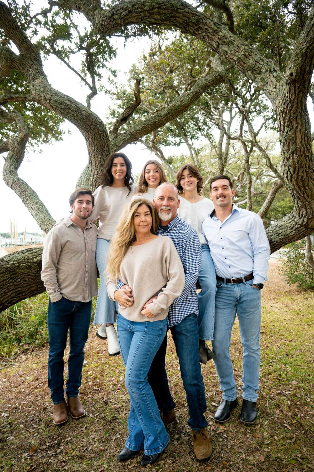 Group standing together by a large oak tree wearing casual sweaters and jeans for an outdoor family photo.