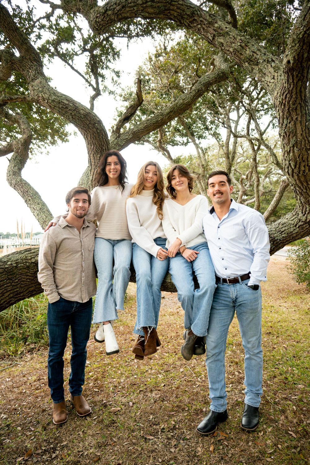 Group posing casually under a sprawling oak tree in coordinated neutral-colored outfits.