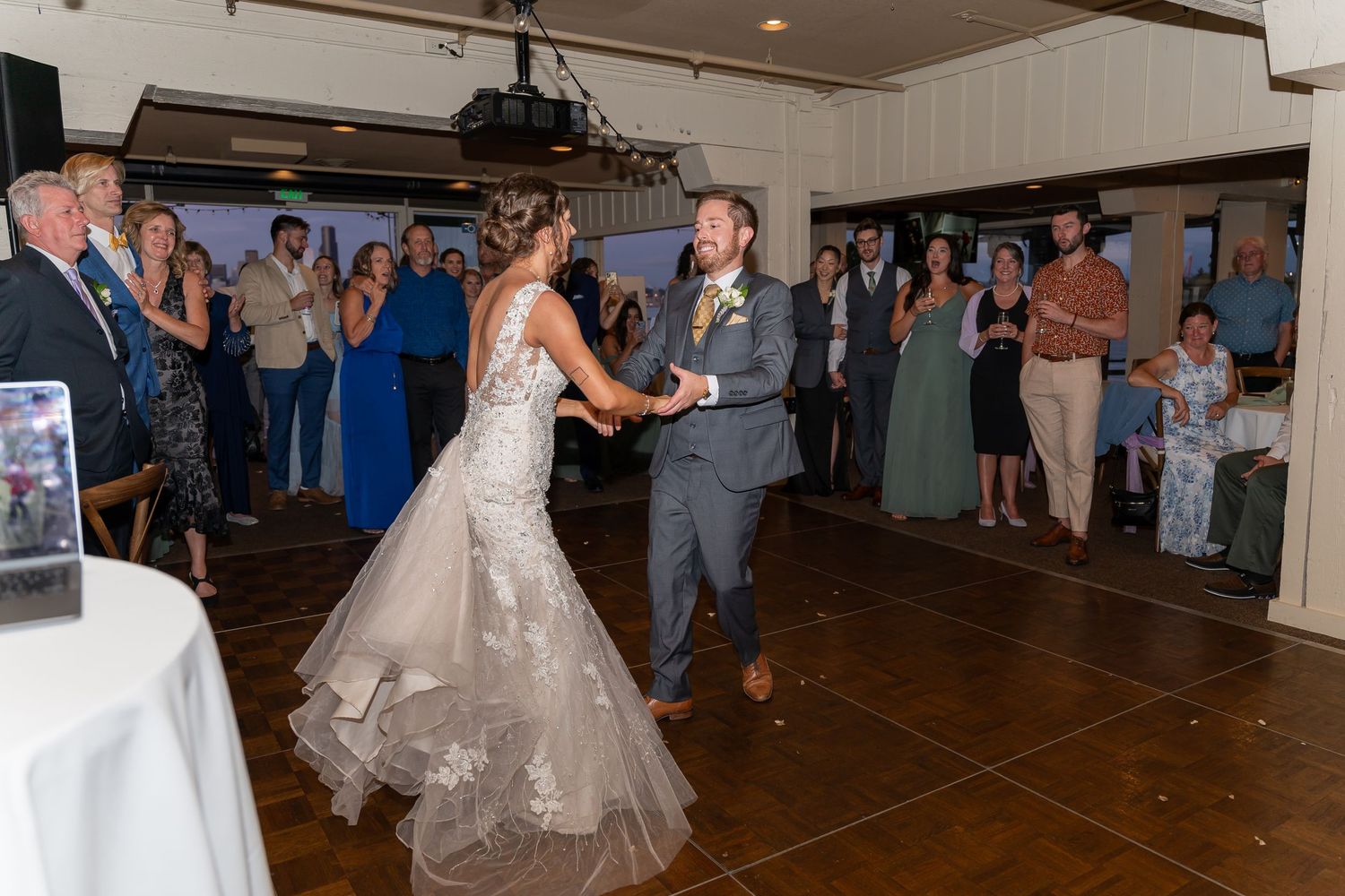 Couple shares their first dance at a wedding reception surrounded by guests watching from the dancefloor edges.