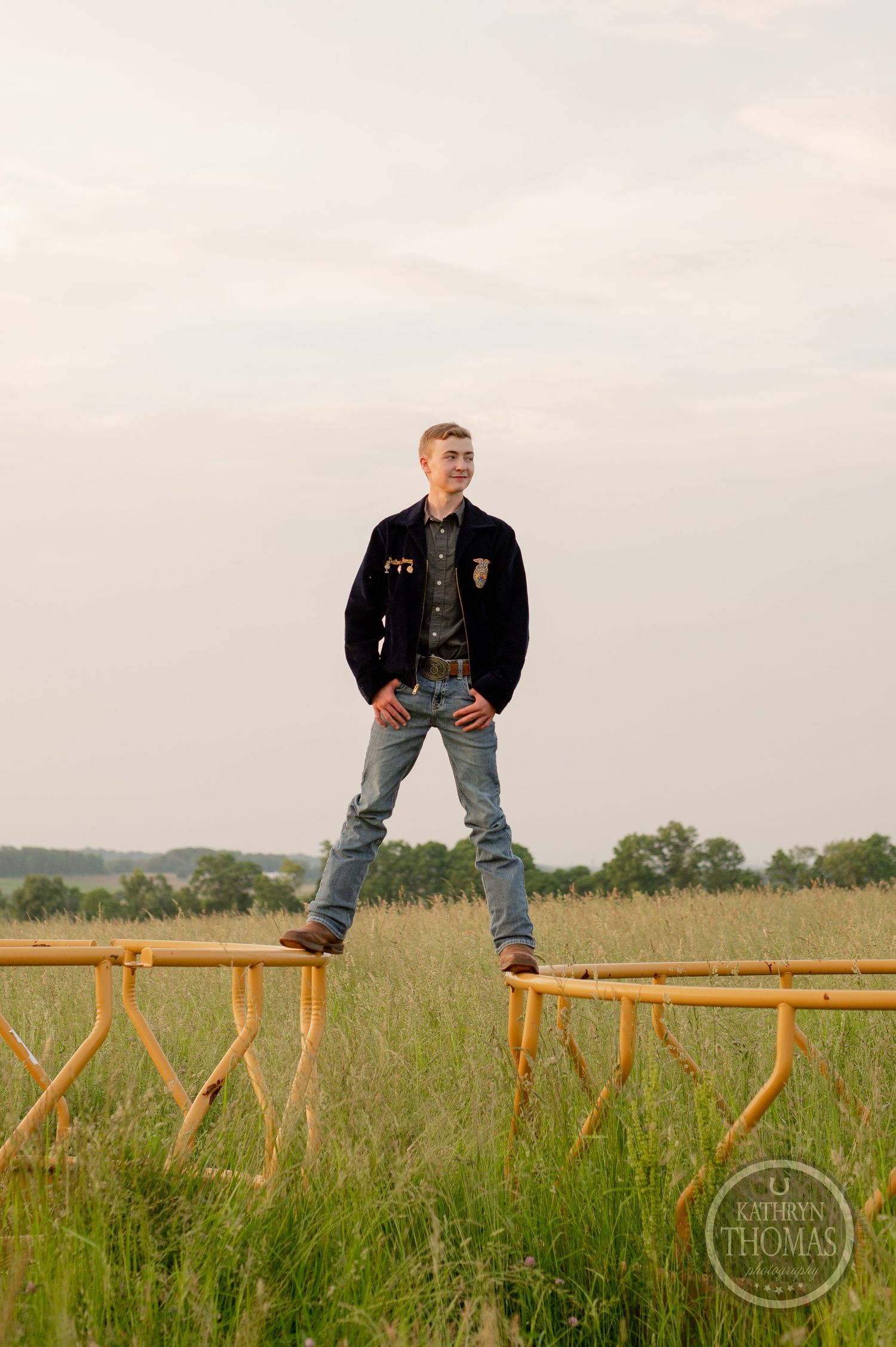 Student in FFA jacket stands confidently on wooden fence with countryside backdrop.