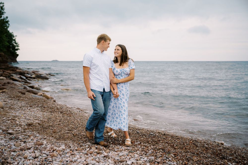 A couple shares a romantic moment on a rocky beach shoreline at dusk.