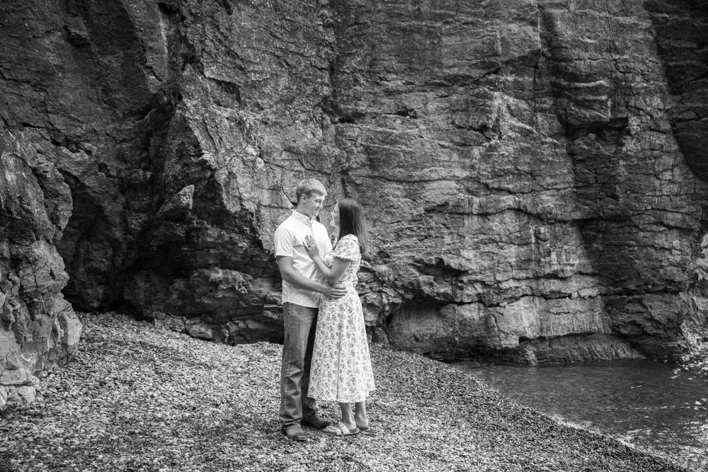 Black and white photo of a couple embracing near dramatic coastal cliffs.