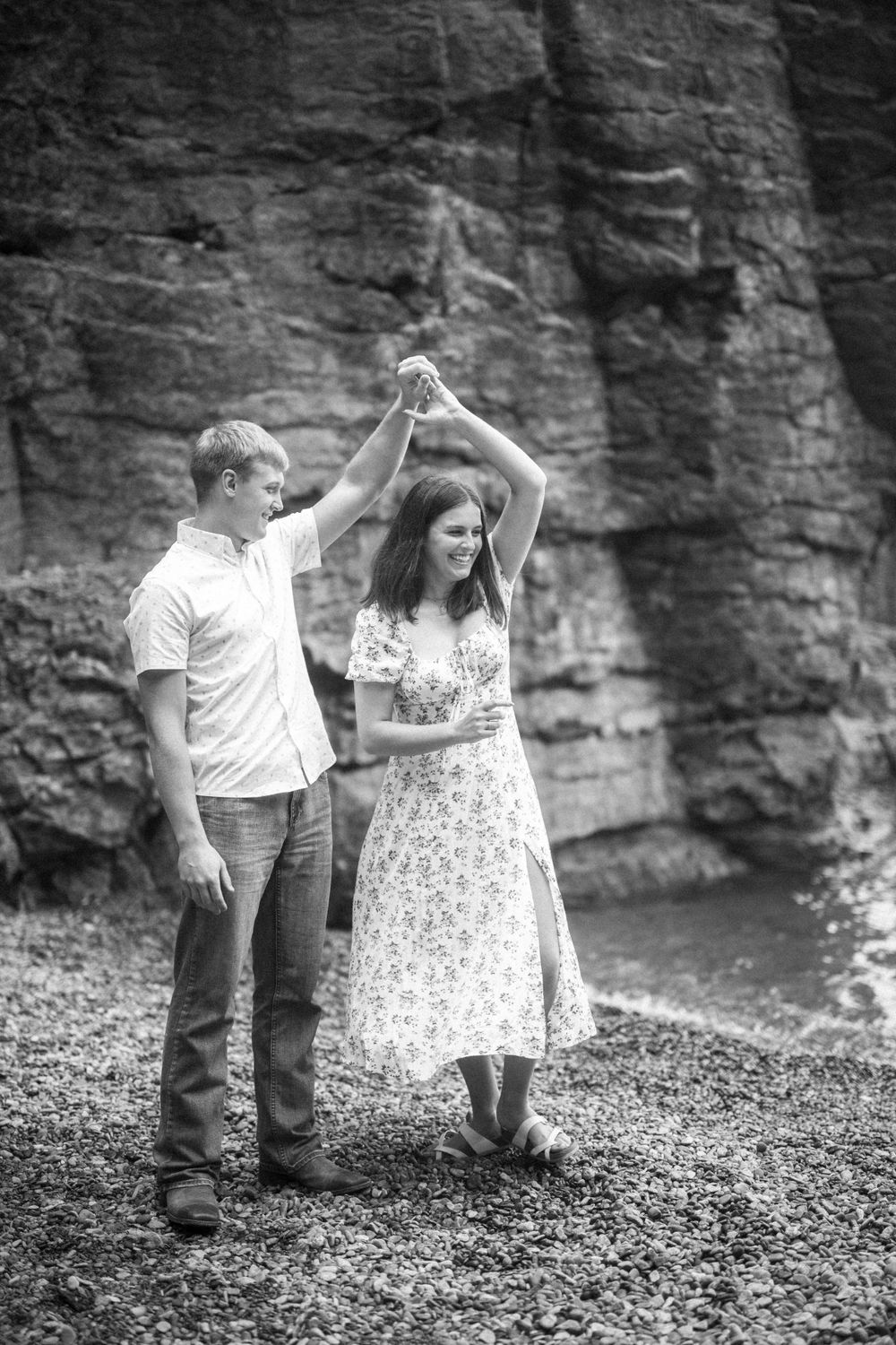 A couple dances together in front of a rocky cliff wall in a romantic black and white portrait.