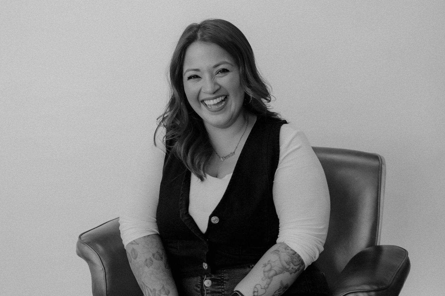 Professional headshot of woman in black vest and white shirt sitting in leather chair.