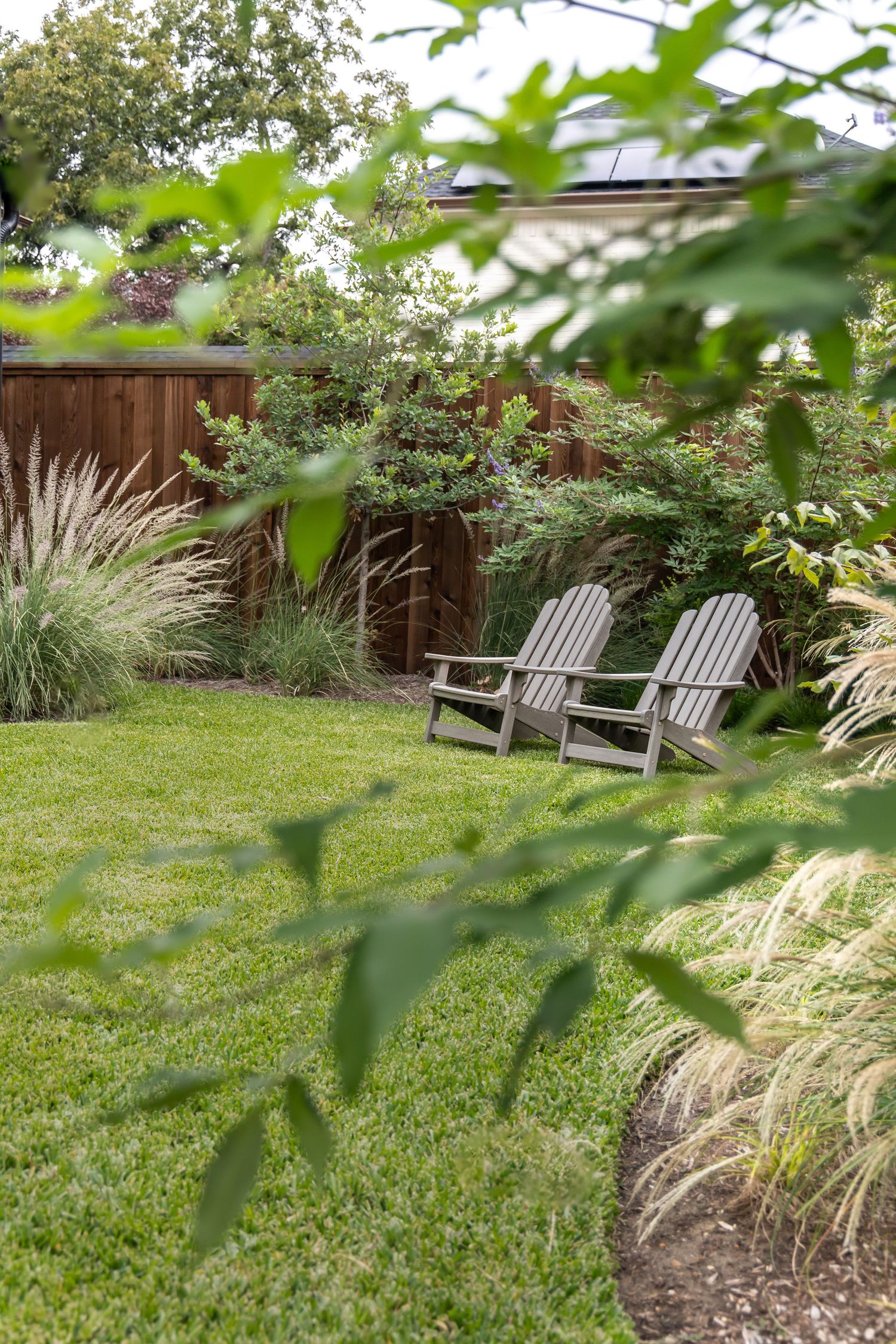 Peaceful backyard garden with Adirondack chairs surrounded by ornamental grasses and lush plants.