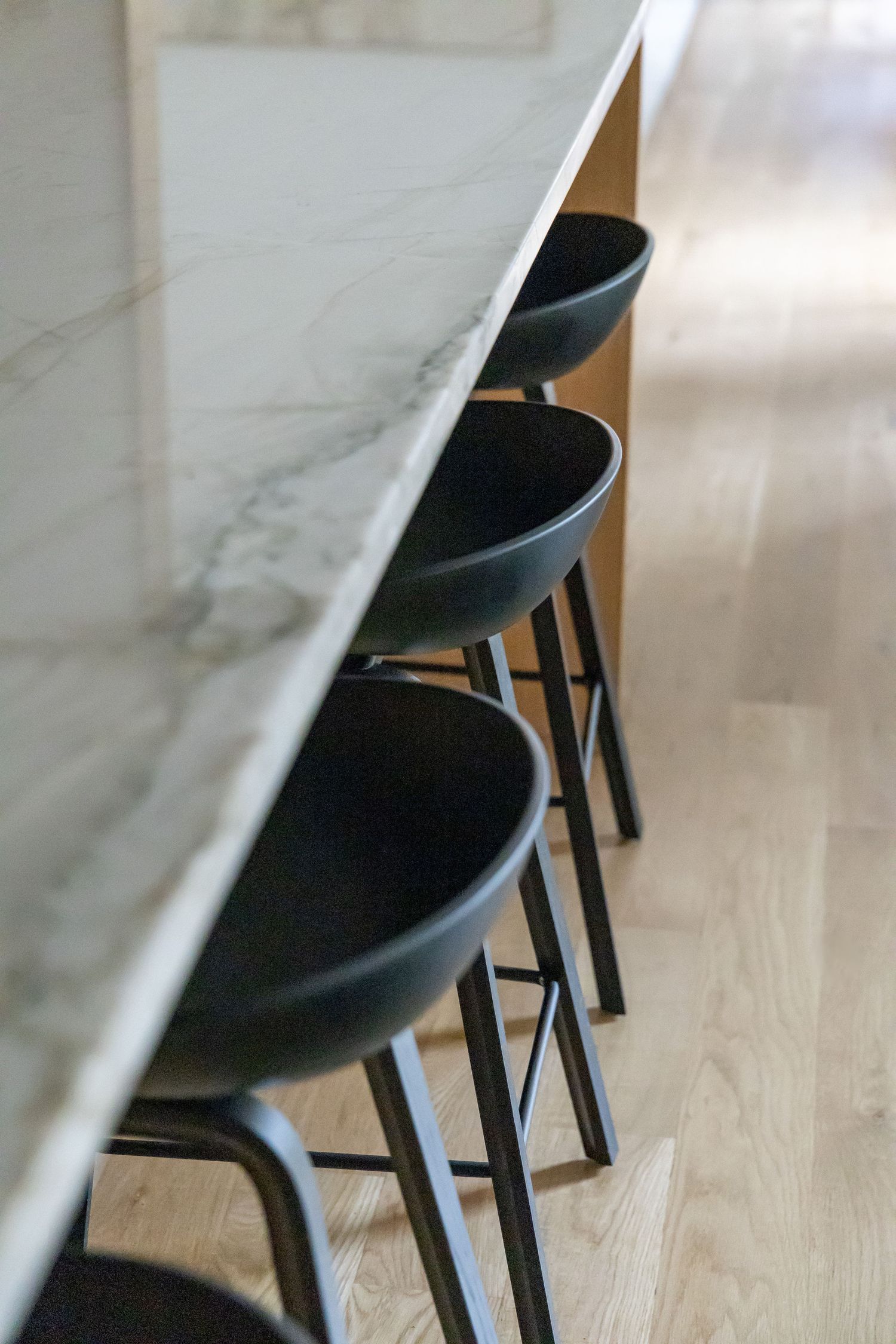 Close-up view of modern black bar stools beneath marble countertop.