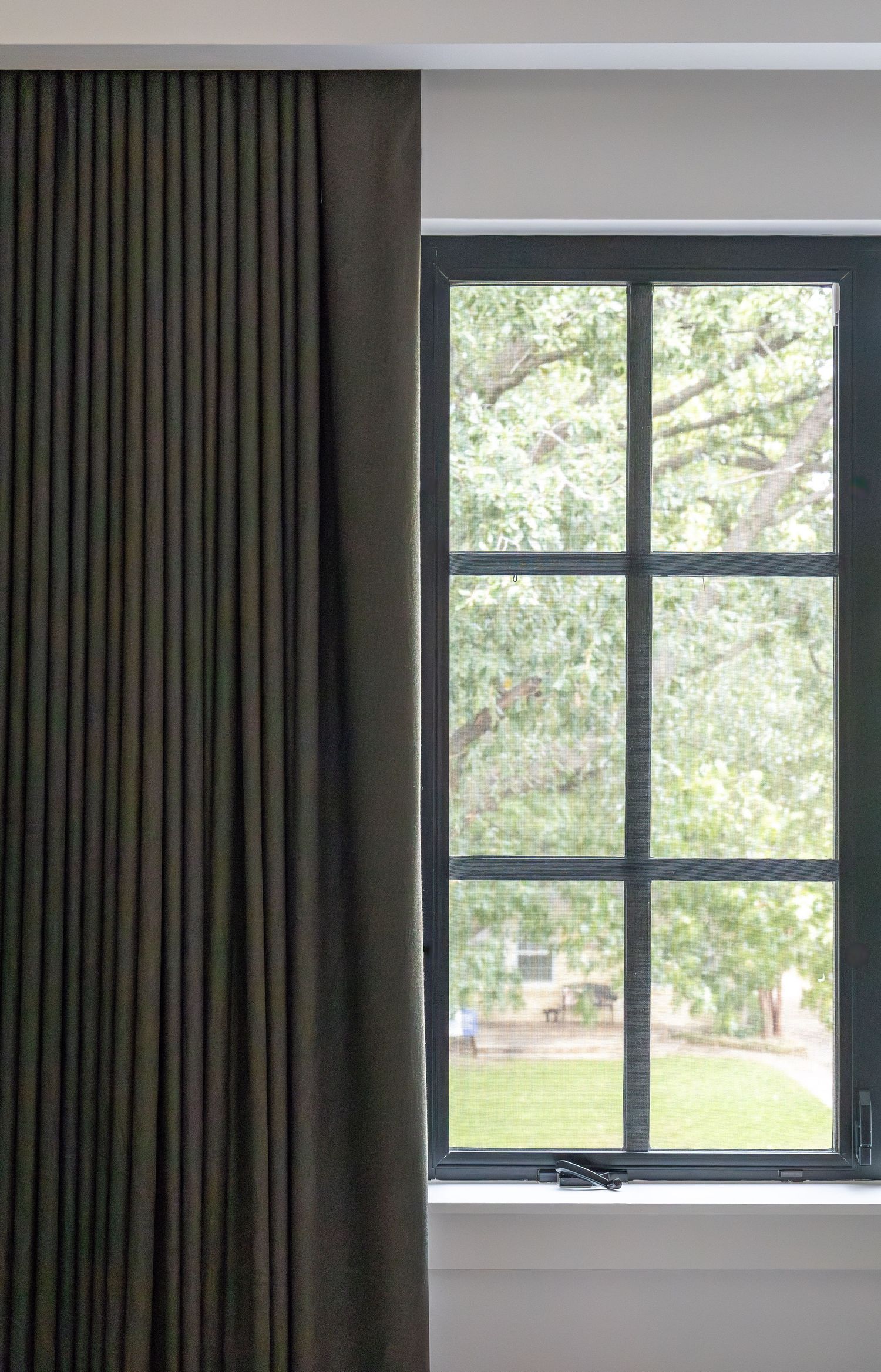 Black-framed window with dark curtains offering a view of green outdoor foliage.
