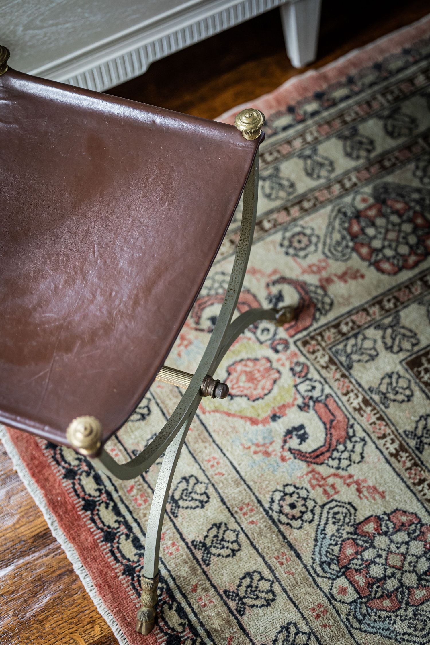 Vintage brown leather chair detail with brass hardware on a decorative oriental rug.