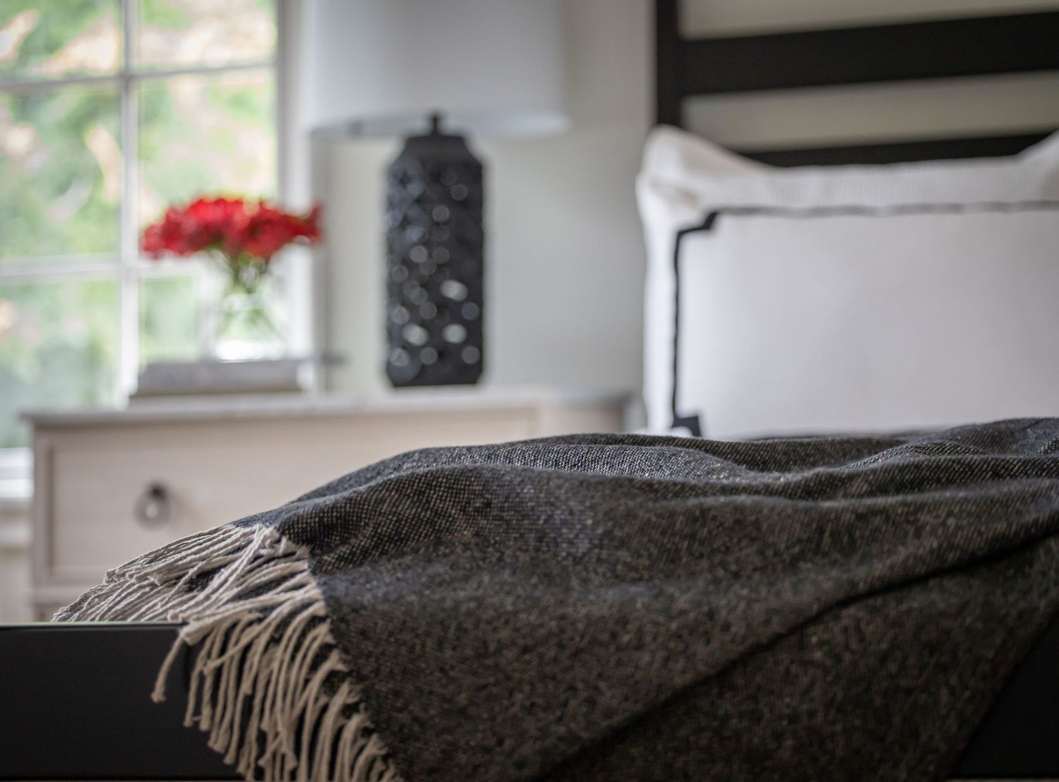 Cozy grey throw blanket draped over furniture near a window with red flowers.