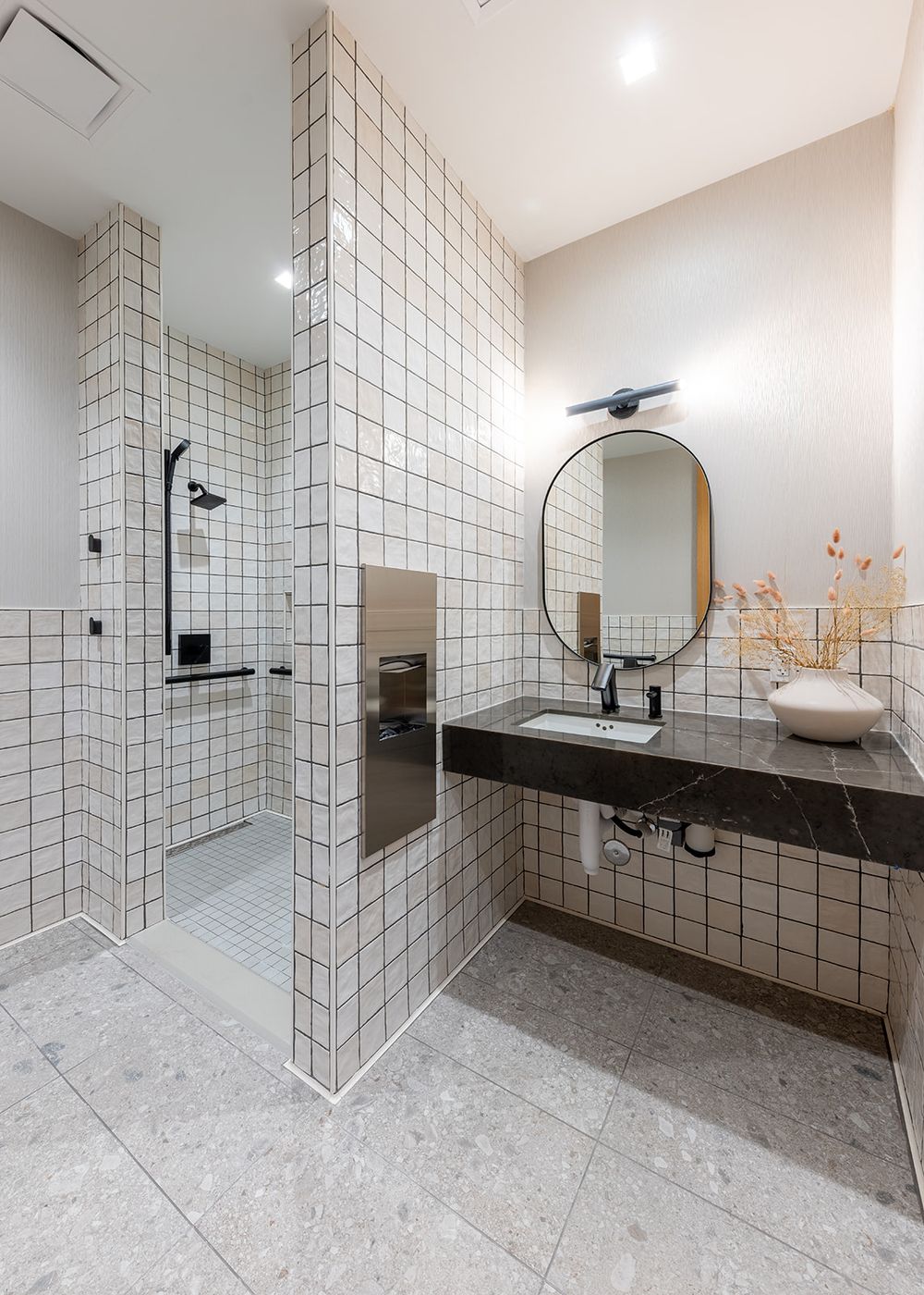 Modern minimalist bathroom with white gridded tile walls, floating vanity, and sleek vessel sink against contrasting dark floor.