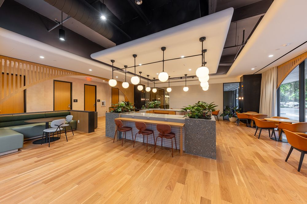 Modern office space featuring exposed ceiling ductwork, pendant lights, and open plan seating areas with wood accents.