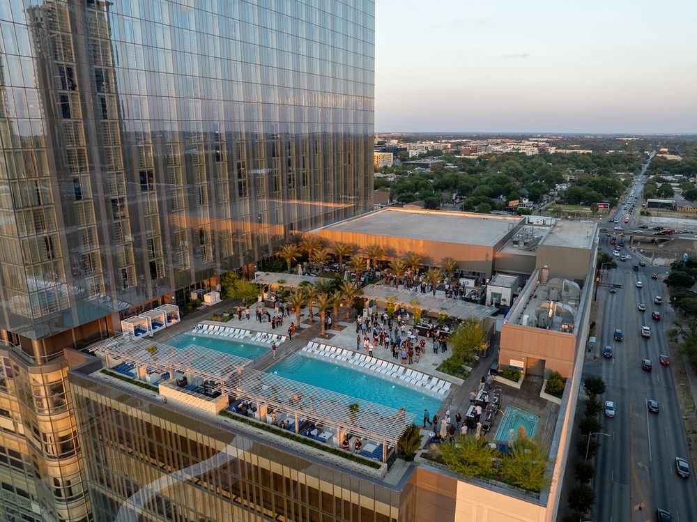 High-rise apartment building rooftop pool deck with crowd gathered for outdoor event during sunset in urban setting.