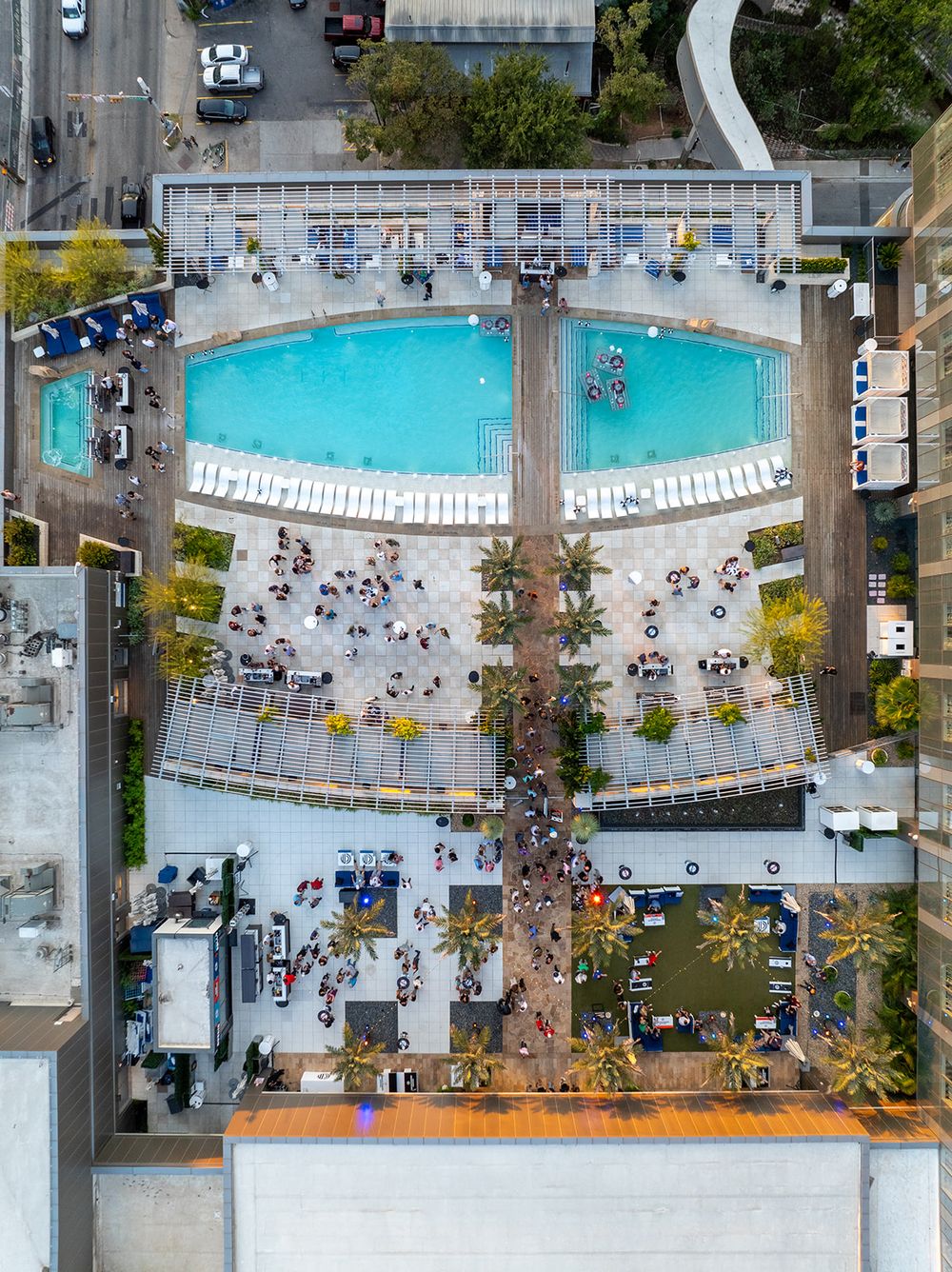 An aerial overhead view of a rooftop pool deck with lounge chairs and palm trees.