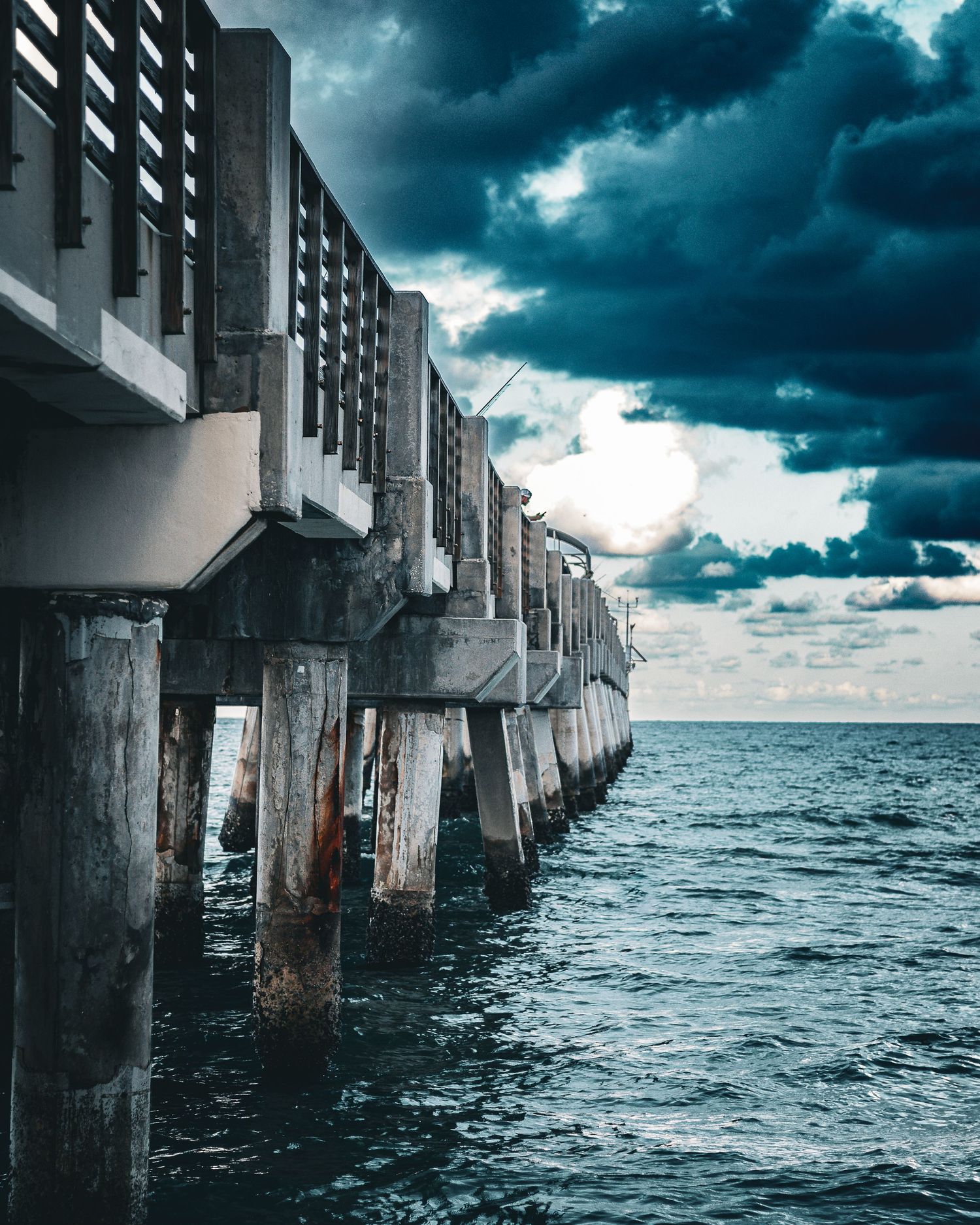 Dark wooden pier extends into turbulent ocean waters under stormy skies.