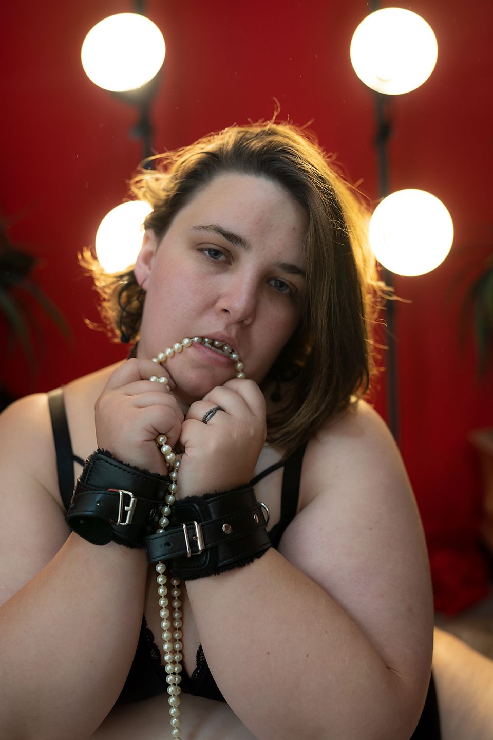 A dramatic boudoir portrait against a red backdrop with dramatic lighting and pearl necklace details.