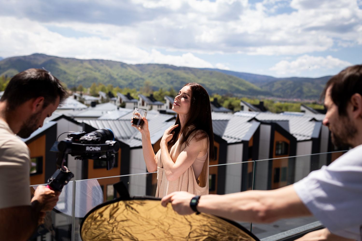 Film crew shooting a woman on a rooftop terrace with stunning mountain scenery behind her.