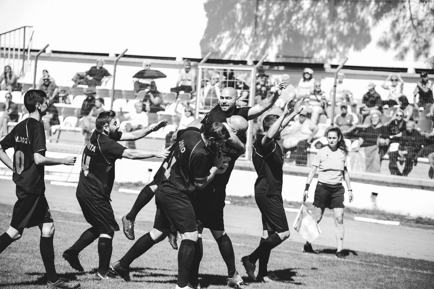 Black and white photo of soccer players celebrating goal together on football pitch with crowd in background.