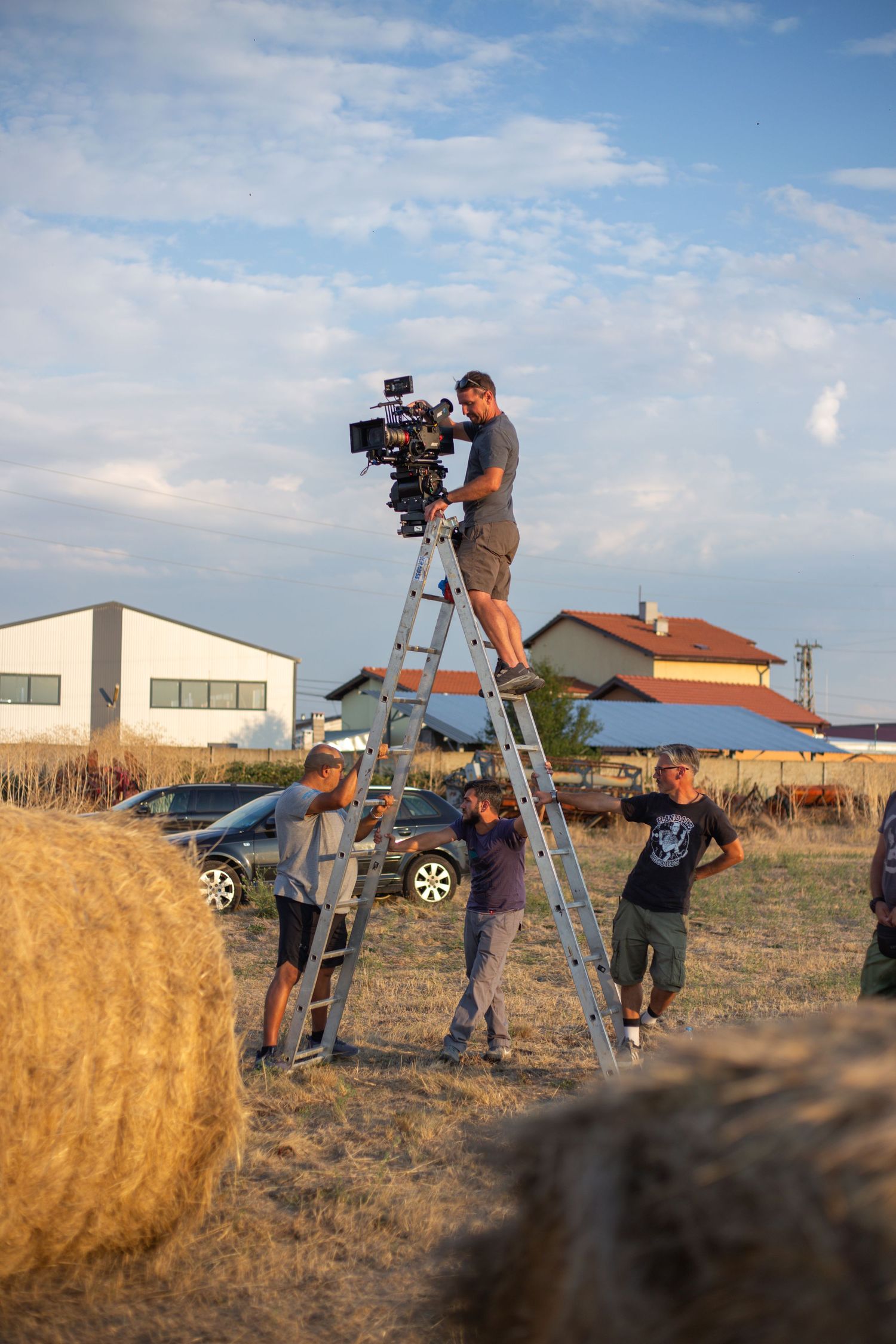 Film crew shooting outdoors on ladders near hay bales at golden hour.