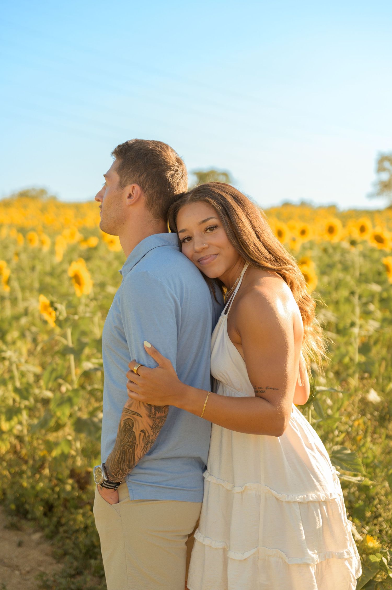 A couple embraces tenderly in a sunlit field of yellow flowers during golden hour.