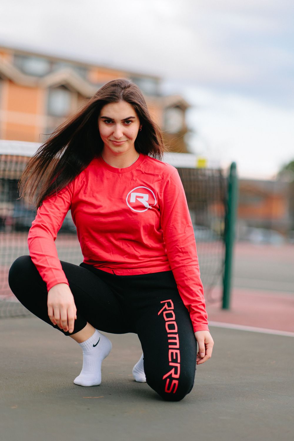 Athletic wear model demonstrates stretching poses on tennis court in red and black outfit.