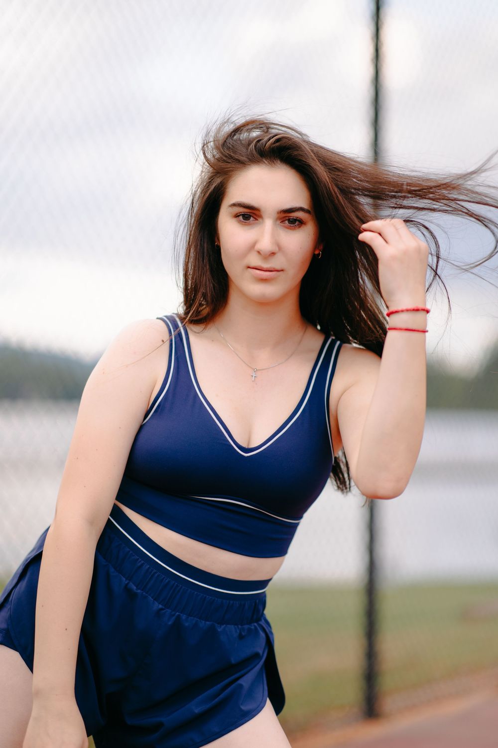 Athletic figure in navy blue sports bra and matching shorts poses outdoors on windy day.