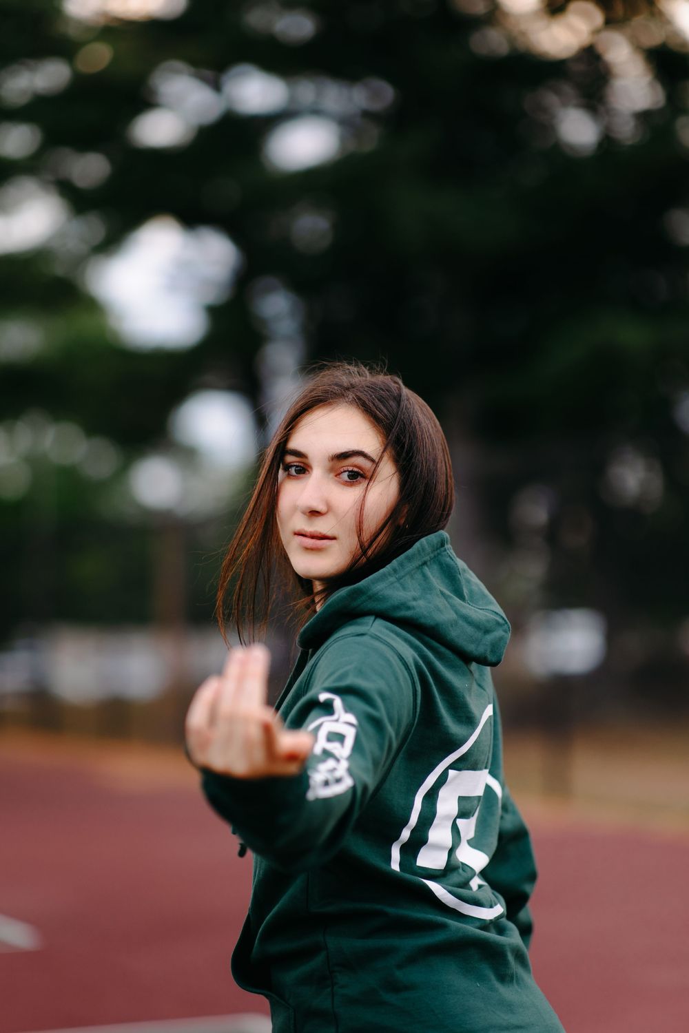 Model in forest green branded hoodie poses on outdoor running track with blurred background.