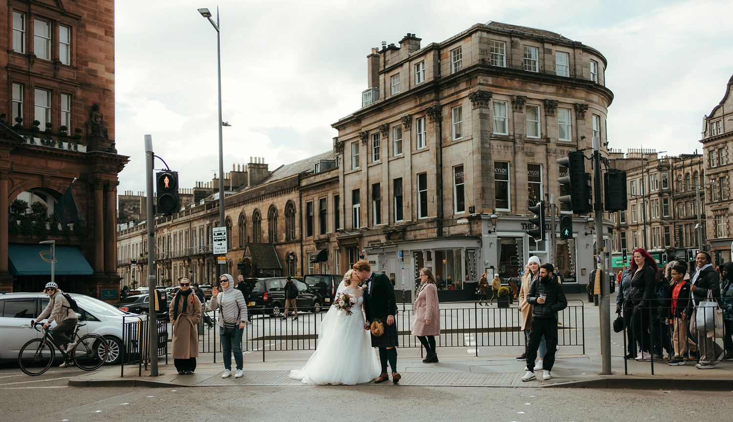 A dramatic black and white wedding photo showing a bride's flowing veil and dress on a city street in front of historic buildings.