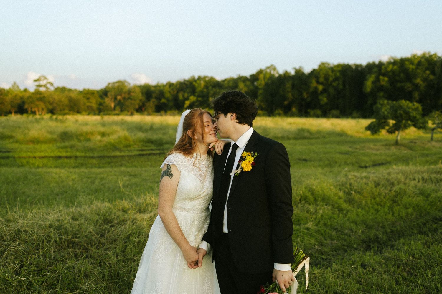 A bride and groom hold hands and nuzzle noses in a field at Congaree and Penn in Jacksonville, FL