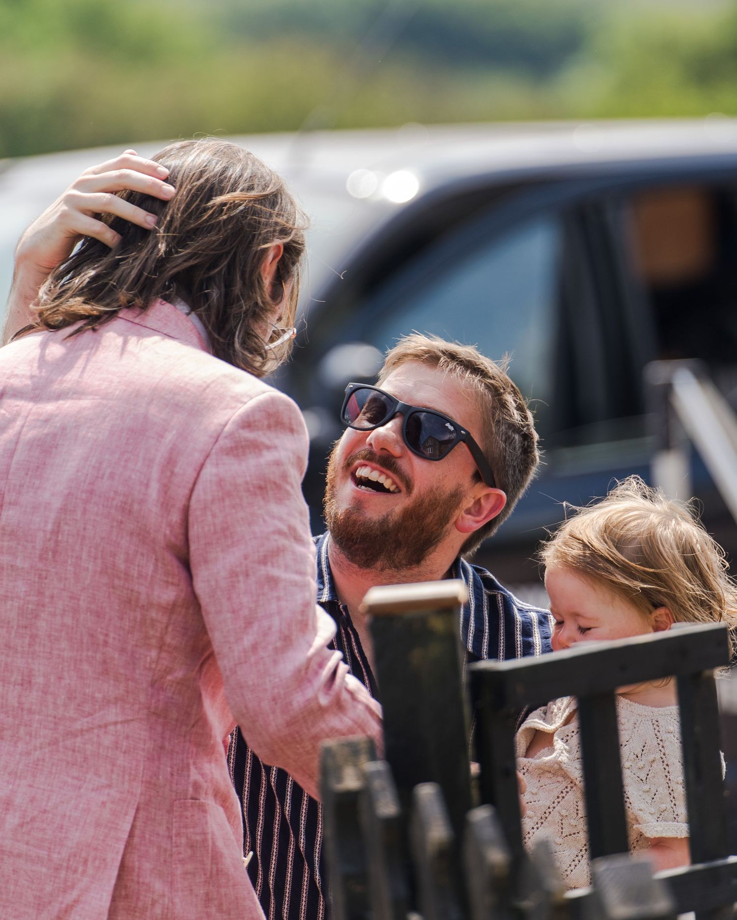 People sharing a joyful moment outdoors while gathered near a car on a sunny day.