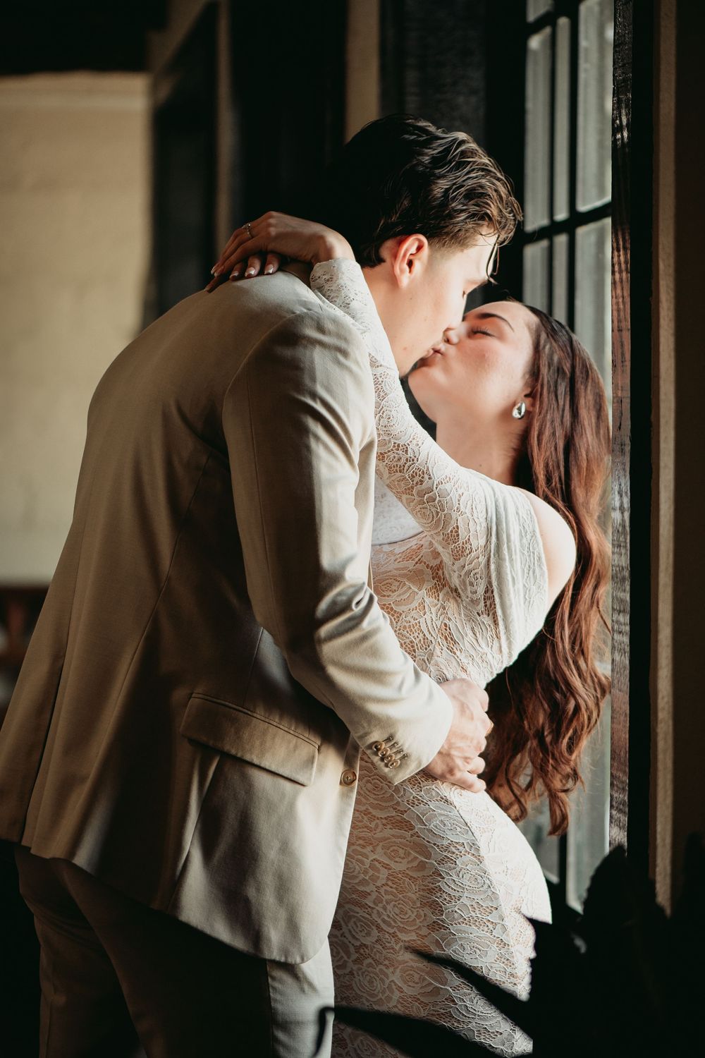 Romantic couple sharing an intimate kiss near a window in soft natural light.