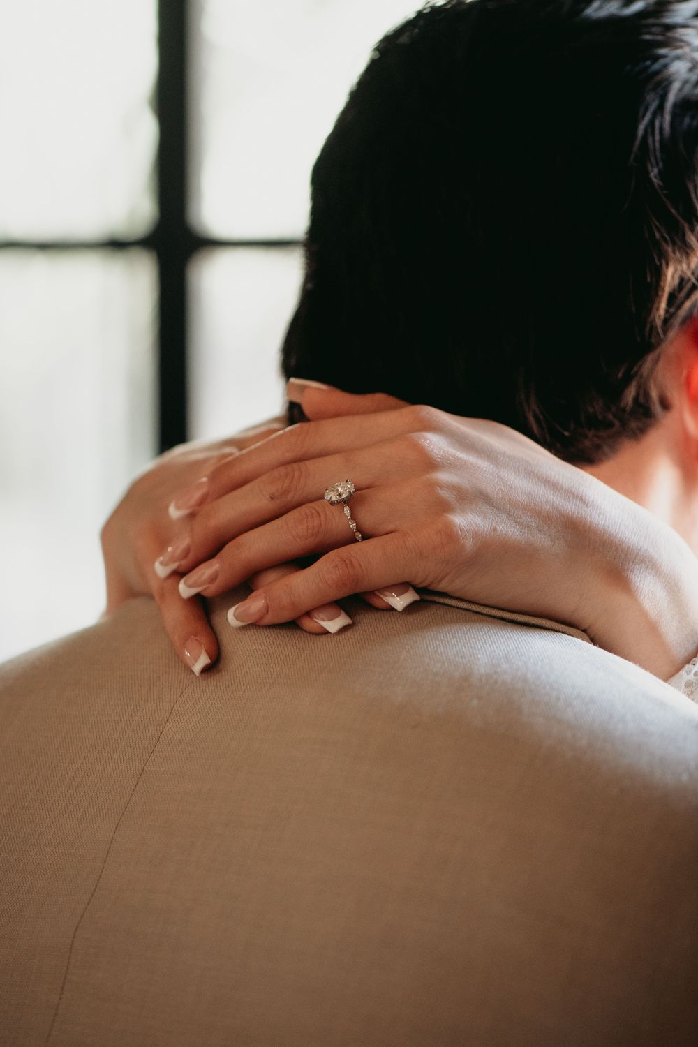 Close up of hands with wedding rings embracing across shoulders in gentle natural light.