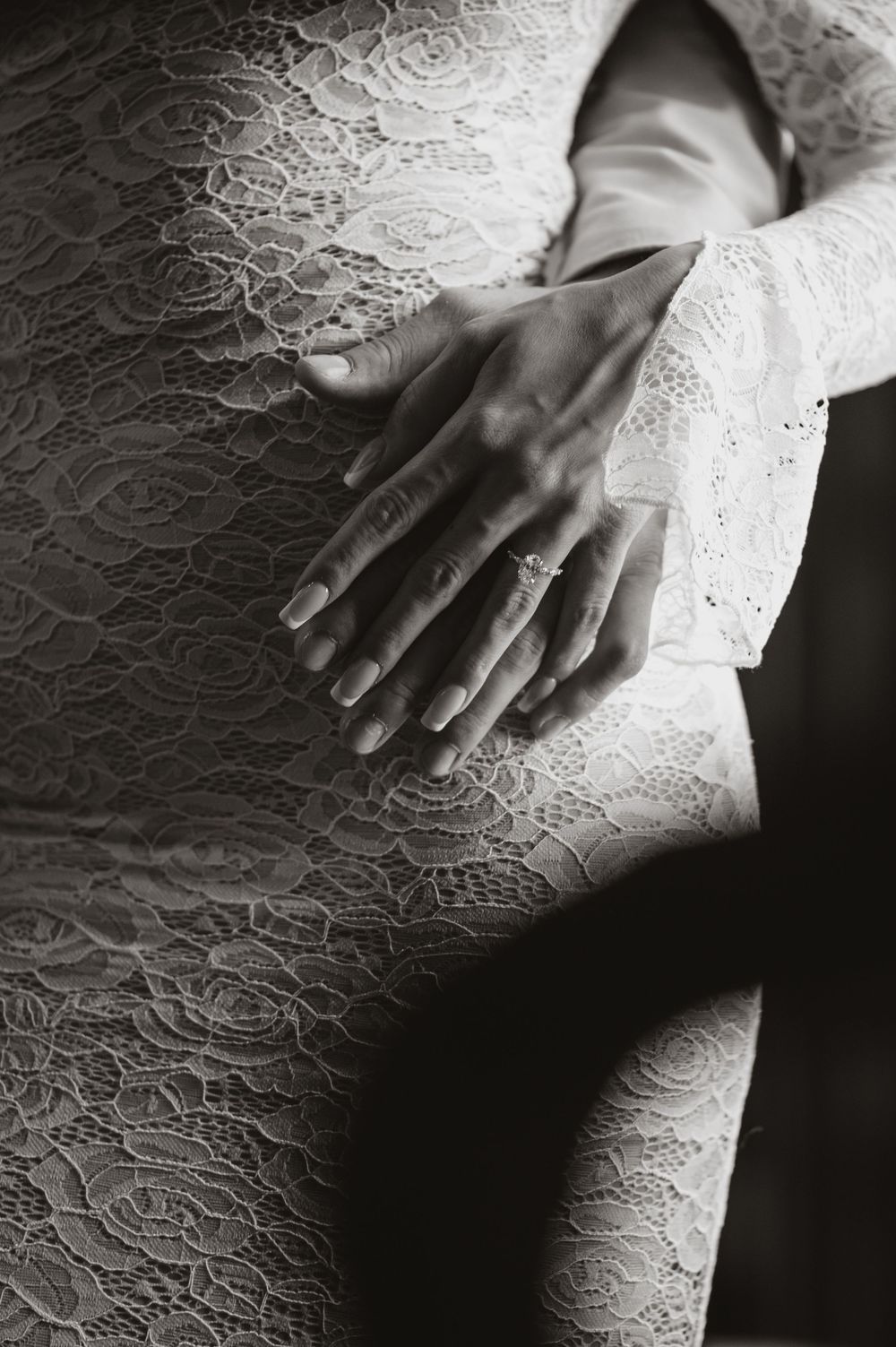 Detail shots of hands against white lace wedding dress fabric in black and white photography.