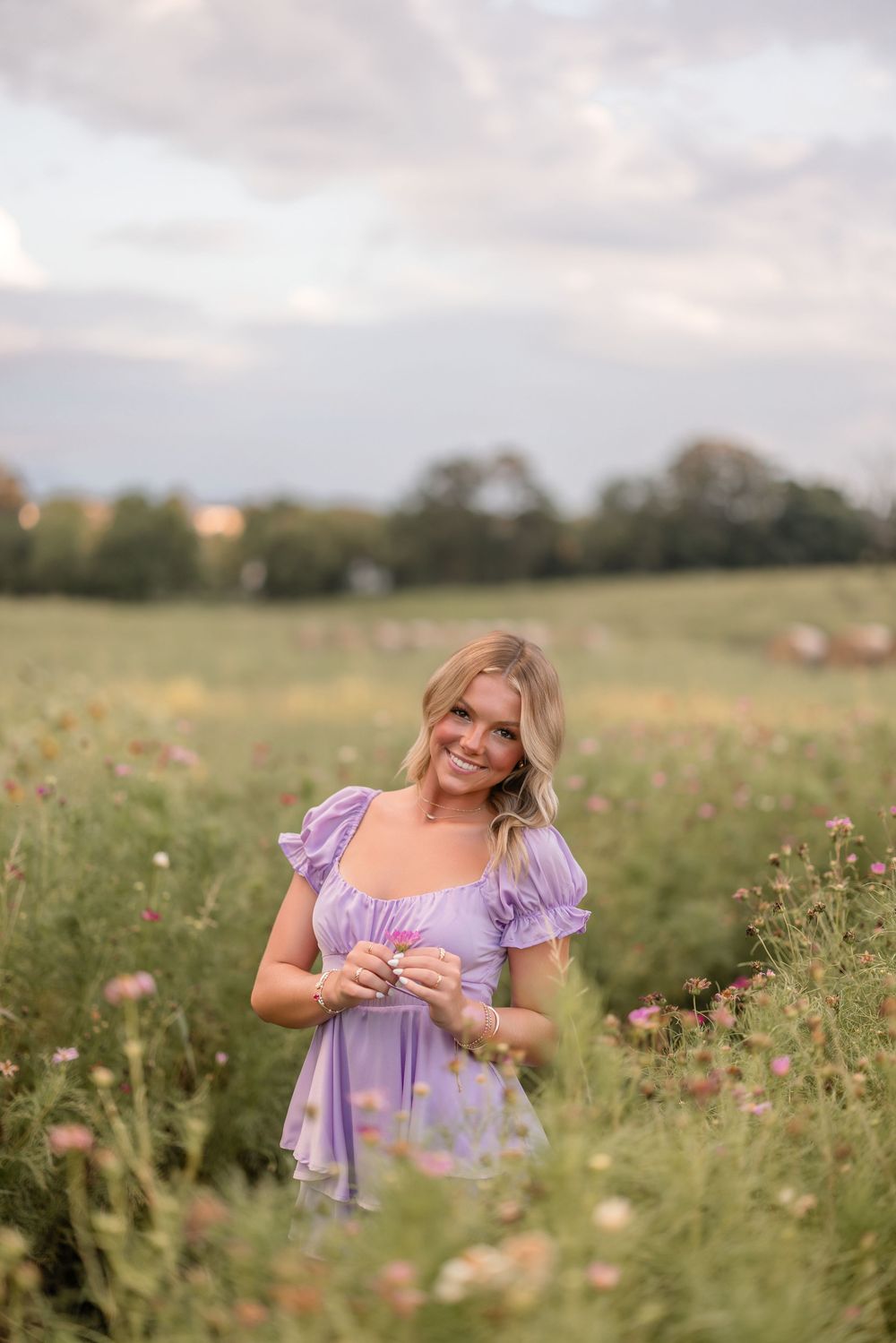 Person in a purple dress stands in a meadow with wildflowers during golden hour sunset.