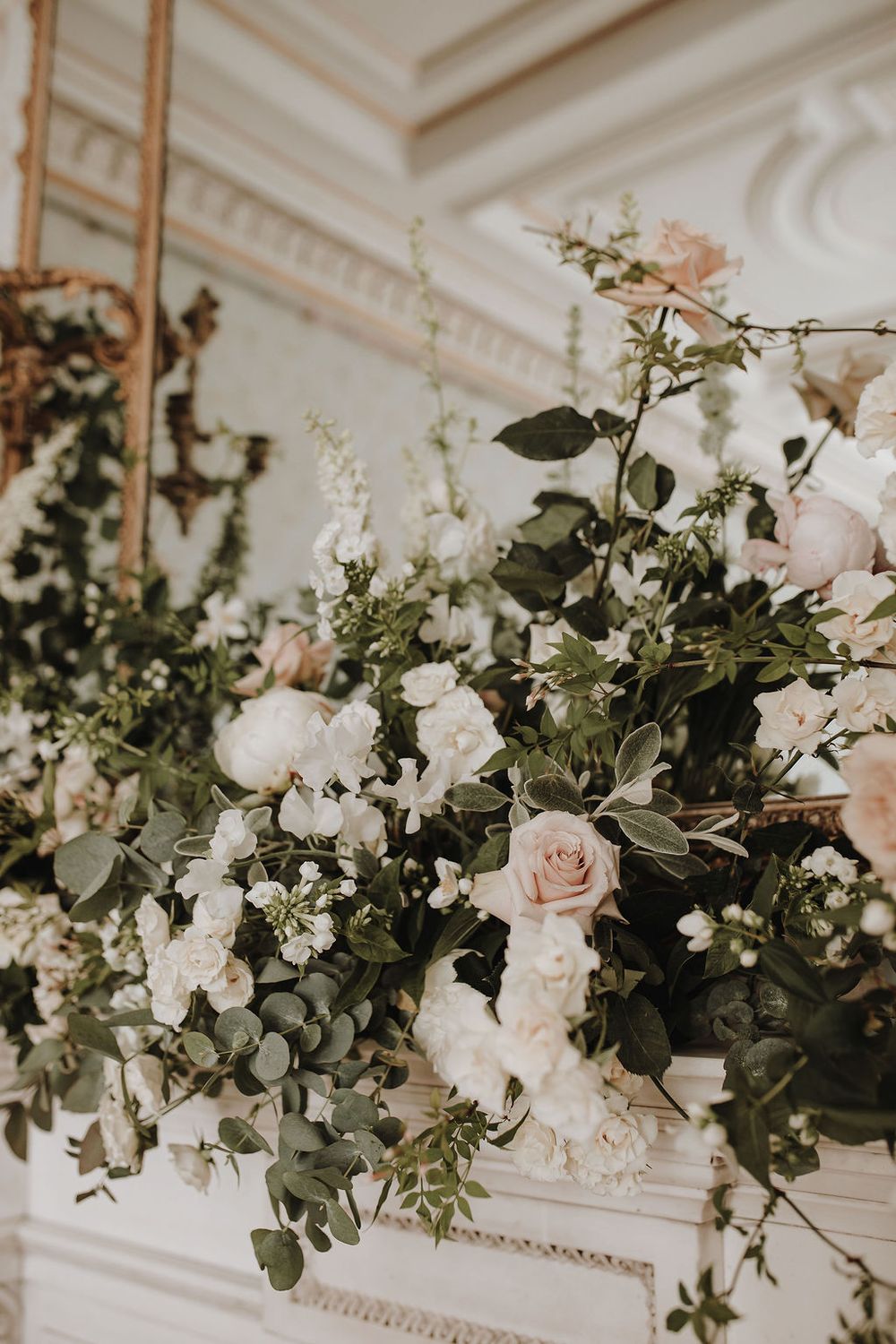 Elegant floral arrangement with blush roses, white flowers and cascading greenery against ornate white molding.