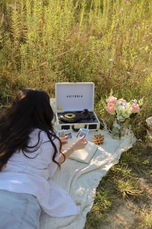 A cozy outdoor picnic setup with books and flowers on a white blanket surrounded by tall grass.