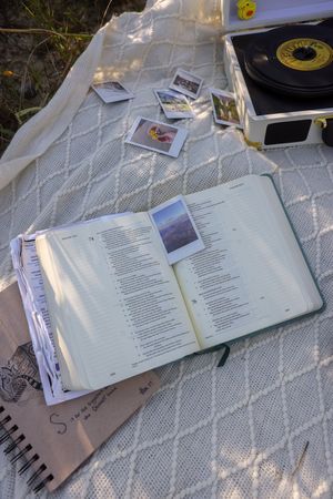 Open books and journals laid out on a white textured blanket in dappled sunlight.