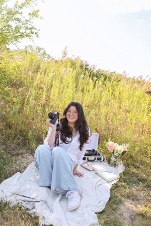 Outdoor photography session setup with blanket, books and flowers in a sunny meadow.