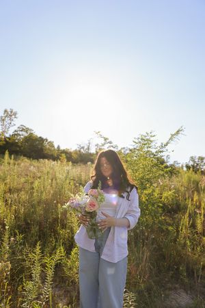 A sunlit silhouette standing in a wildflower field holding a bouquet at golden hour.