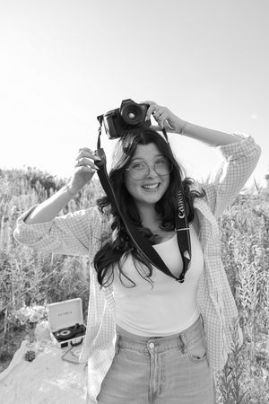 A candid black and white photo showing someone with a camera and plaid shirt in a meadow.