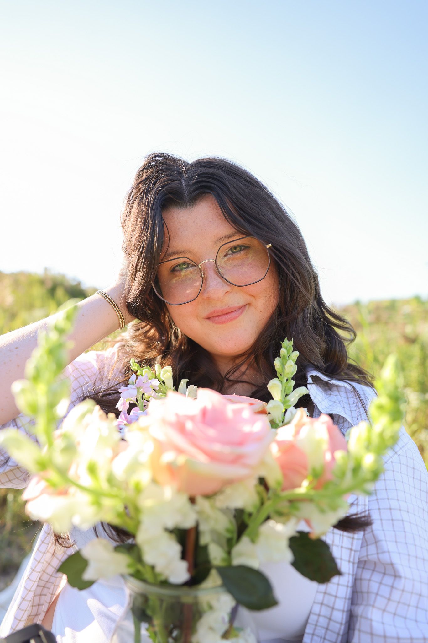 A joyful portrait in a field holding a bouquet of pink and white flowers on a sunny day.