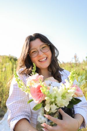 A cheerful outdoor portrait with glasses holding a fresh bouquet of pink and white flowers.