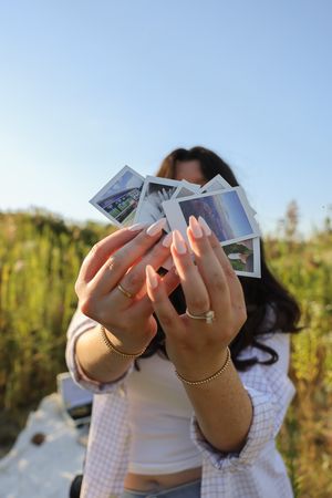 Hands holding up polaroid photos against a blue sky in an outdoor setting.