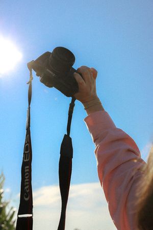 A hand holds up a camera against bright blue sky and sunlight.