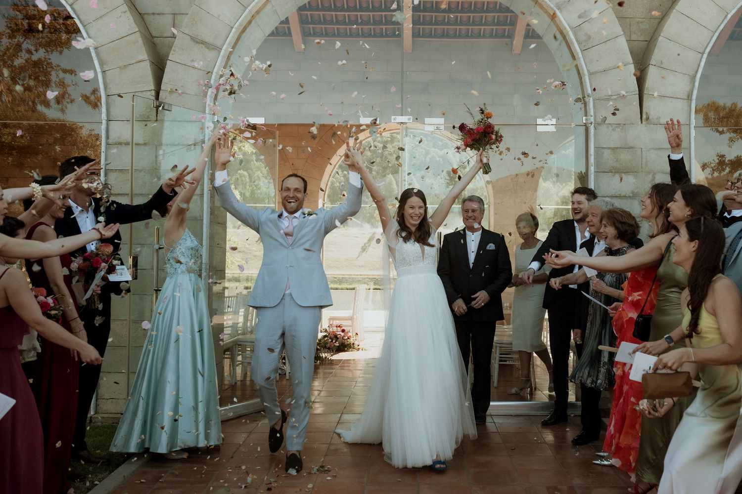 A joyous celebration in an arched venue with confetti and guests celebrating a wedding ceremony.