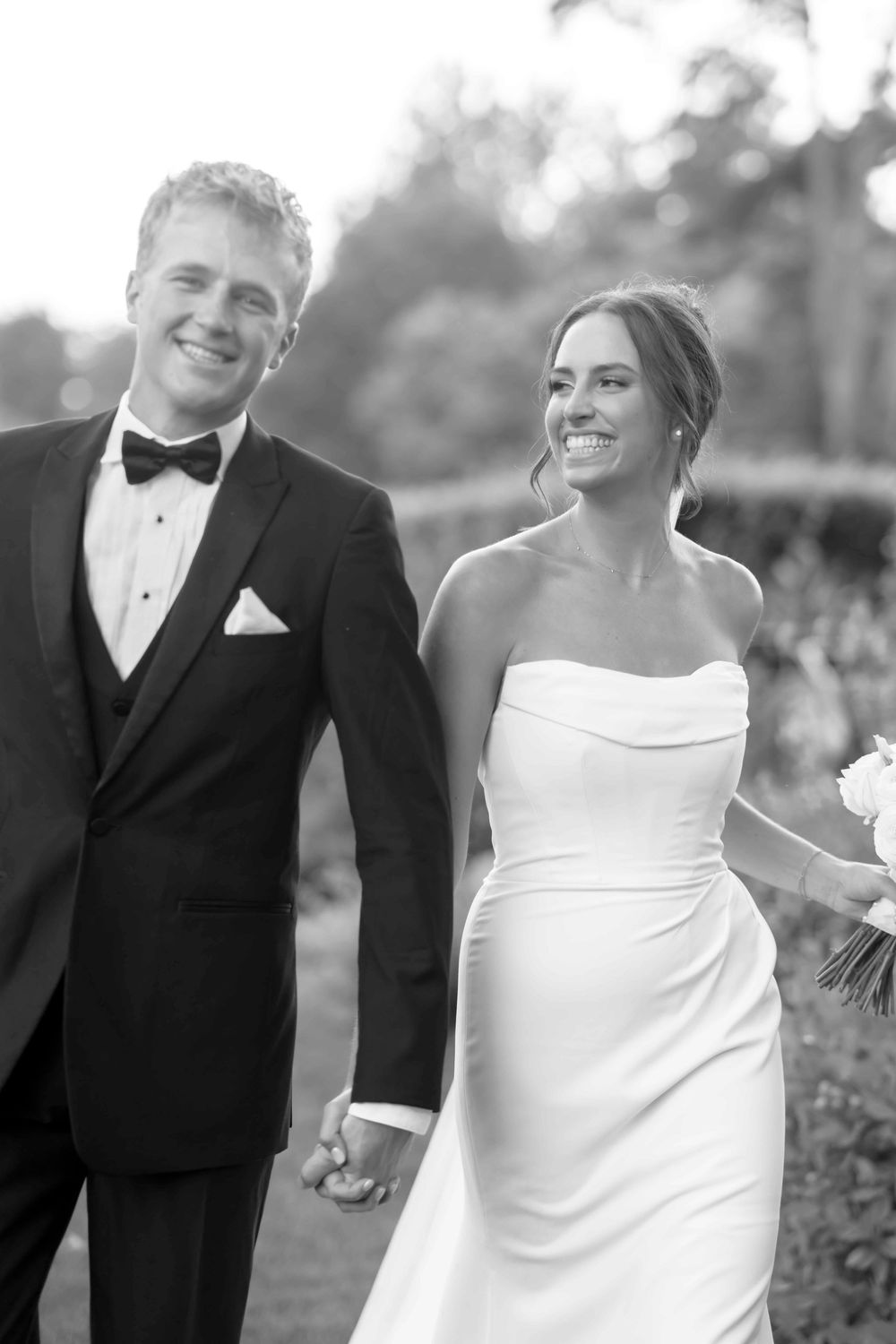 Black and white photo of newlyweds laughing together outdoors in formal wedding attire.
